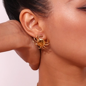 Close-up of a gold crab-shaped stud earring worn on ear showing detailed metal texture