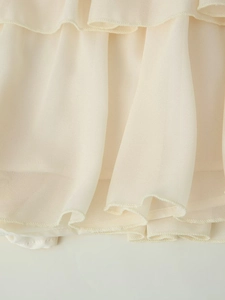 Dettaglio di tessuto in chiffon a balze multistrato con bordi ondulati color crema