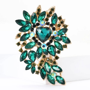 Close-up of golden brooch featuring heart-shaped green crystal and leaf patterns