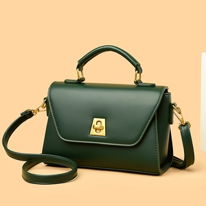 Chic dark green crossbody flap bag with gold lock and adjustable strap on beige background