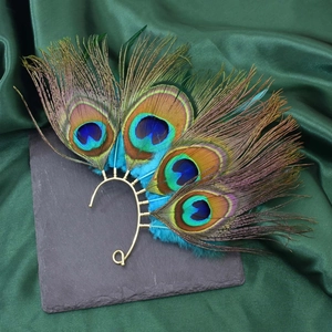 Detail of natural peacock feather ear cuff with golden frame on dark stone background