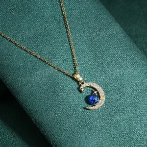 Golden moon pendant necklace with zircons and blue stone on green textured fabric