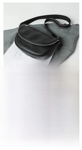 Detail view of black semi-circular PU crossbody bag with striped fabric shoulder strap