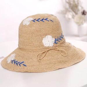 Detailed close-up of beige raffia sun hat featuring white 3D flowers and blue embroidery