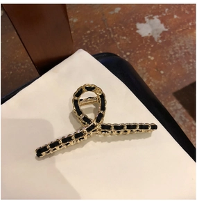 Close-up of golden metal hair claw with black ribbon woven chain design for women