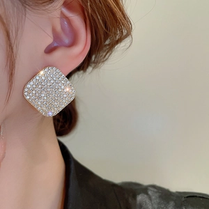 Close-up of elegant square gold stud earrings with pavé crystals on a female model