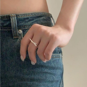 Close-up of minimalist silver double-cross knot ring on finger with denim background