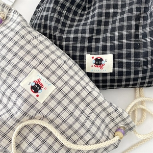 Detail of checkered drawstring backpacks in black and white with cat embroidery