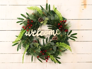 Close-up of pine needle wreath with red berries and a wooden Welcome sign on white wood