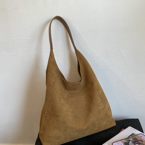 Brown faux suede hobo shoulder bag set against a minimalist white wall background
