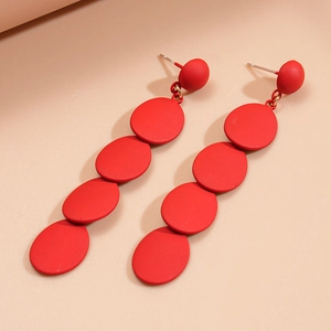 Detail view of red matte geometric oval drop earrings on a soft beige background