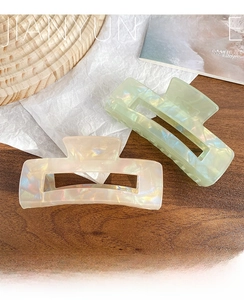 Detail of two iridescent acetate hair claws in cream and mint green on a rustic table