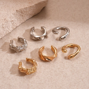 Three-piece metallic irregular geometric ear cuffs in silver and gold on a stone background