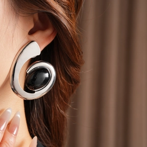 Detail of a silver spiral earring with a black oval gemstone worn by a model