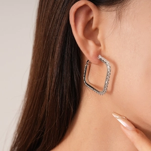 Detailed close-up of square silver-colored hoop earrings with pavé rhinestones on a model