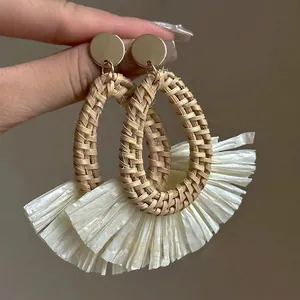 Detailed shot of handmade bohemian gold studs with woven raffia tassel and natural fiber