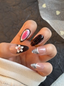 Detail showing press-on nails with 3D white flowers, amber textures, and zebra patterns