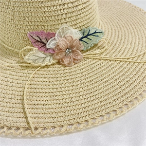 Close-up of beige straw hat featuring lace flower, 3D mesh petals, and a crystal center