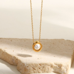 Dettaglio di una collana dorata minimalista con ciondolo ad anello ondulato e perla bianca