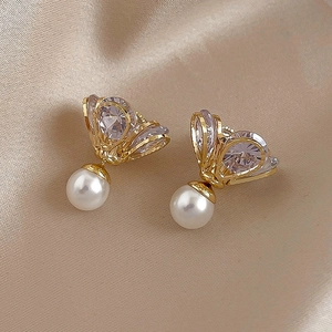 Detail of golden bow earrings with sparkling cubic zirconia and elegant white pearls