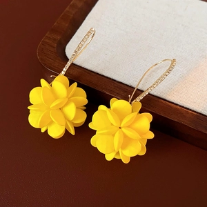 Dettaglio di orecchini a fiore in acrilico giallo con strass su vassoio di legno