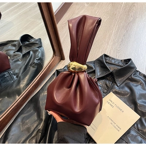 Detail of burgundy drawstring bucket bag with unique large gold-tone metal knot handle