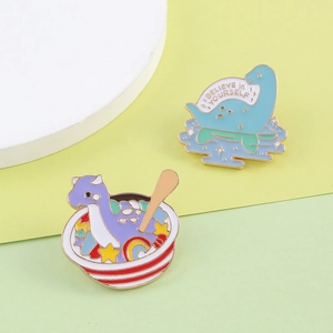 Set of two cute enamel dinosaur pins with Believe in Yourself text on a yellow background