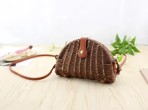 Detail of dark brown semi-circle straw crossbody bag with leather buckle on wood