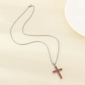 Silver stainless steel tennis necklace with red crystal cross pendant on beige surface