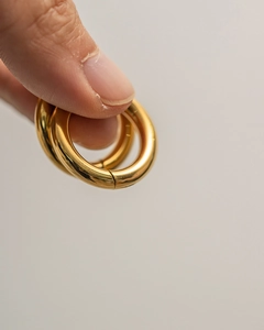 Detailed close-up of shiny gold double-layered stainless steel hoop earrings held by fingers