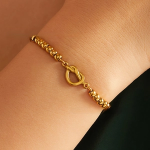 Close-up of a 4mm gold beaded bracelet with a center knot clasp worn on a female wrist