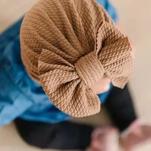 Detail of a brown ribbed knit baby turban hat featuring a large decorative bow
