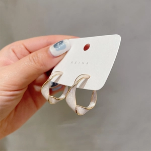Close-up of twisted gold-edged geometric hoop earrings with white enamel finish