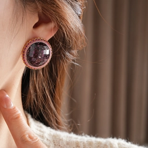 Detail of round resin stud earring with purple glitter and golden crystal trim on model