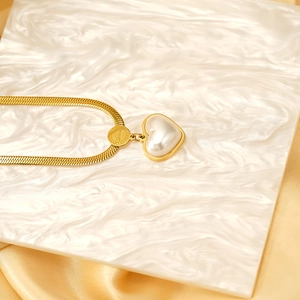 Elegante collana con ciondolo a cuore dorato, catena a serpente e perla su sfondo di seta