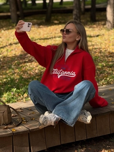 Close-up of red oversized sweatshirt with California print in an autumn forest setting