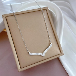 Macro view of silver V-shaped pendant with inset crystals on a golden textured box