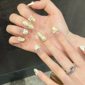 Detail of cream white press-on nails with 3D bows, gold glitter, and rhinestones