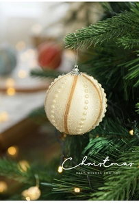 Detail of ivory Christmas ball with glitter and pearls on a lit tree branch