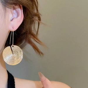 Close-up of golden round earrings with concentric ripple texture worn by a model