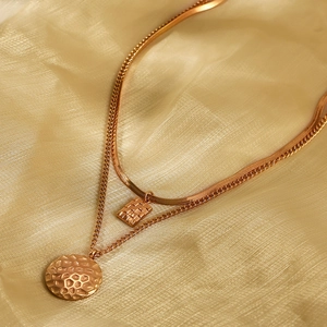 Detail of double-layer gold necklace with textured square and round pendants on silk