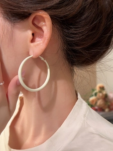 Close-up of a model wearing large cream enamel hoop earrings with a matte finish