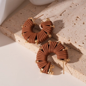 Detail of brown leather wrapped U-shaped earrings with golden bead accents on stone