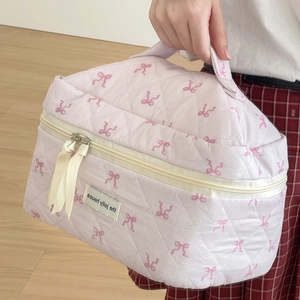 Quilted pink makeup bag with red bow pattern and top handle shown in a lifestyle setting