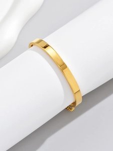 Polished gold wide surface cuff bracelet displayed on a white cylindrical stand