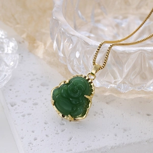 Macro shot of gold-tone Buddha pendant with emerald green faux jade finish on white surface
