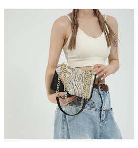 Chic black and gold shoulder bag with marble pattern and gold chain strap on model