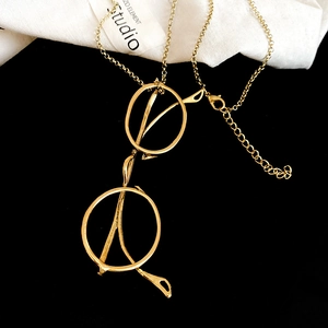 Detail of a golden glasses-shaped pendant necklace on a minimalist black and white background