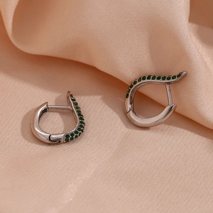Detail of silver hoop earring with green zircon stones on soft silk fabric background
