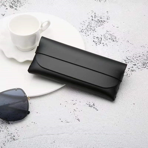 Minimalist black PVC leather sunglasses pouch with strap closure on a stone texture